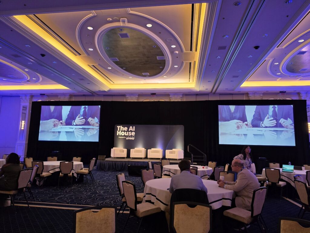 Zaal van AI House tijdens de Ai4-week in Las Vegas met podium en twee grote schermen