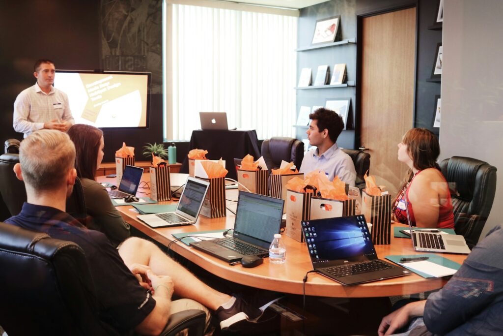 Man geeft uitleg aan een groep collega's met laptops in een kantoorruimte