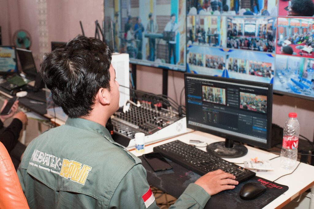 Persoon in uniform die beeld- en geluidsapparatuur bedient achter meerdere schermen